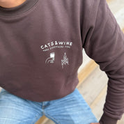 Person wearing a brown sweatshirt with 'Cats & Wine Make Everything Fine' text and graphics.